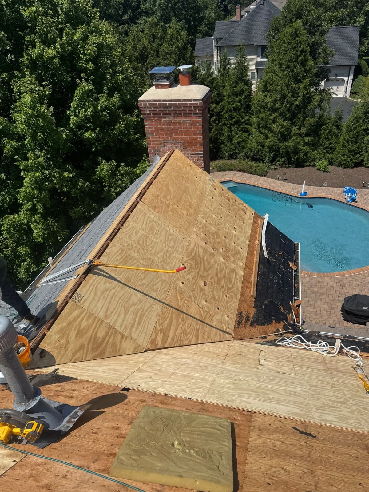 New plywood roof decking cut in tight around a brick chimney on a New Jersey re-roof, the old covering stripped off the adjoining slope
