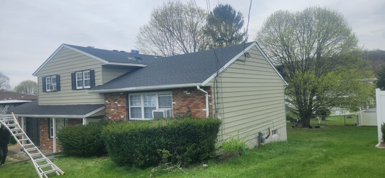 Postwar New Jersey split-level finished in dark architectural asphalt shingle after a full tear-off, main roof, dormered upper storey and lower wing all re-covered