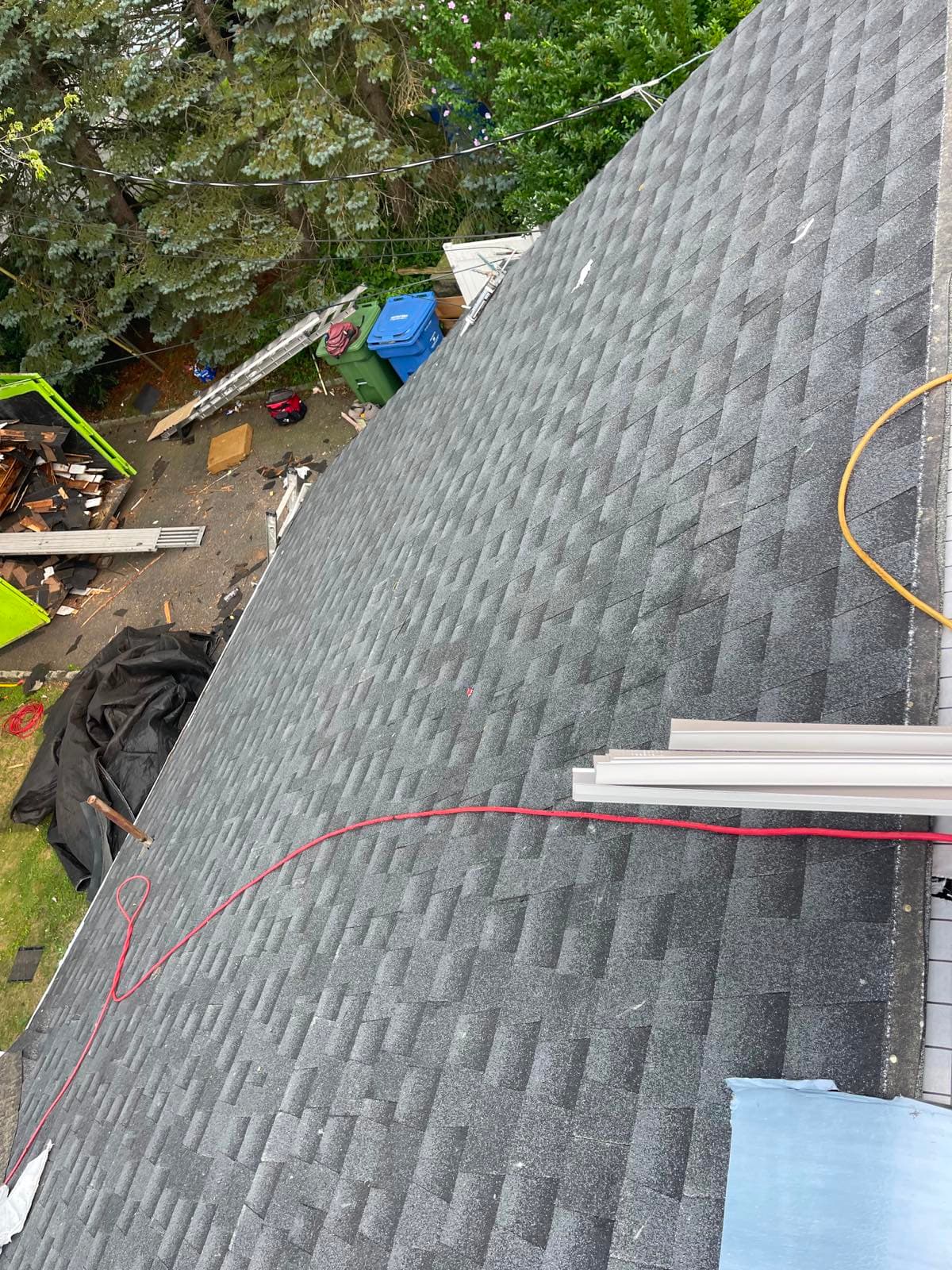 Freshly laid charcoal architectural asphalt shingles running down the hip of a Parlin, NJ roof, with the tear-off dumpster, ladder and tarped landscaping visible in the yard below
