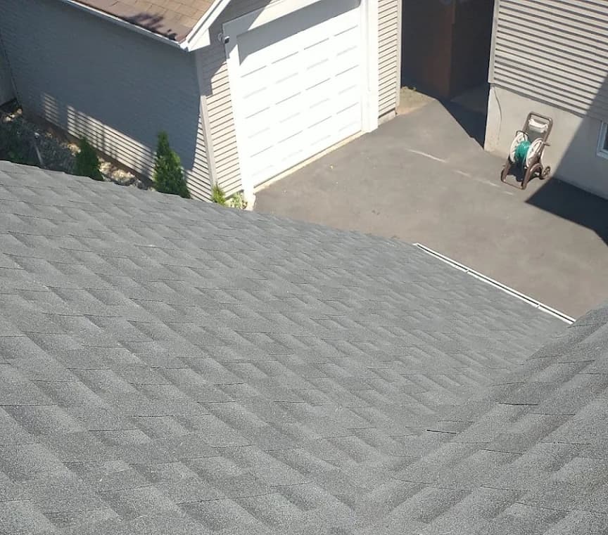 Finished light grey architectural asphalt shingle roof plane on a Rutherford, NJ home, with new white drip edge along the eave above the driveway