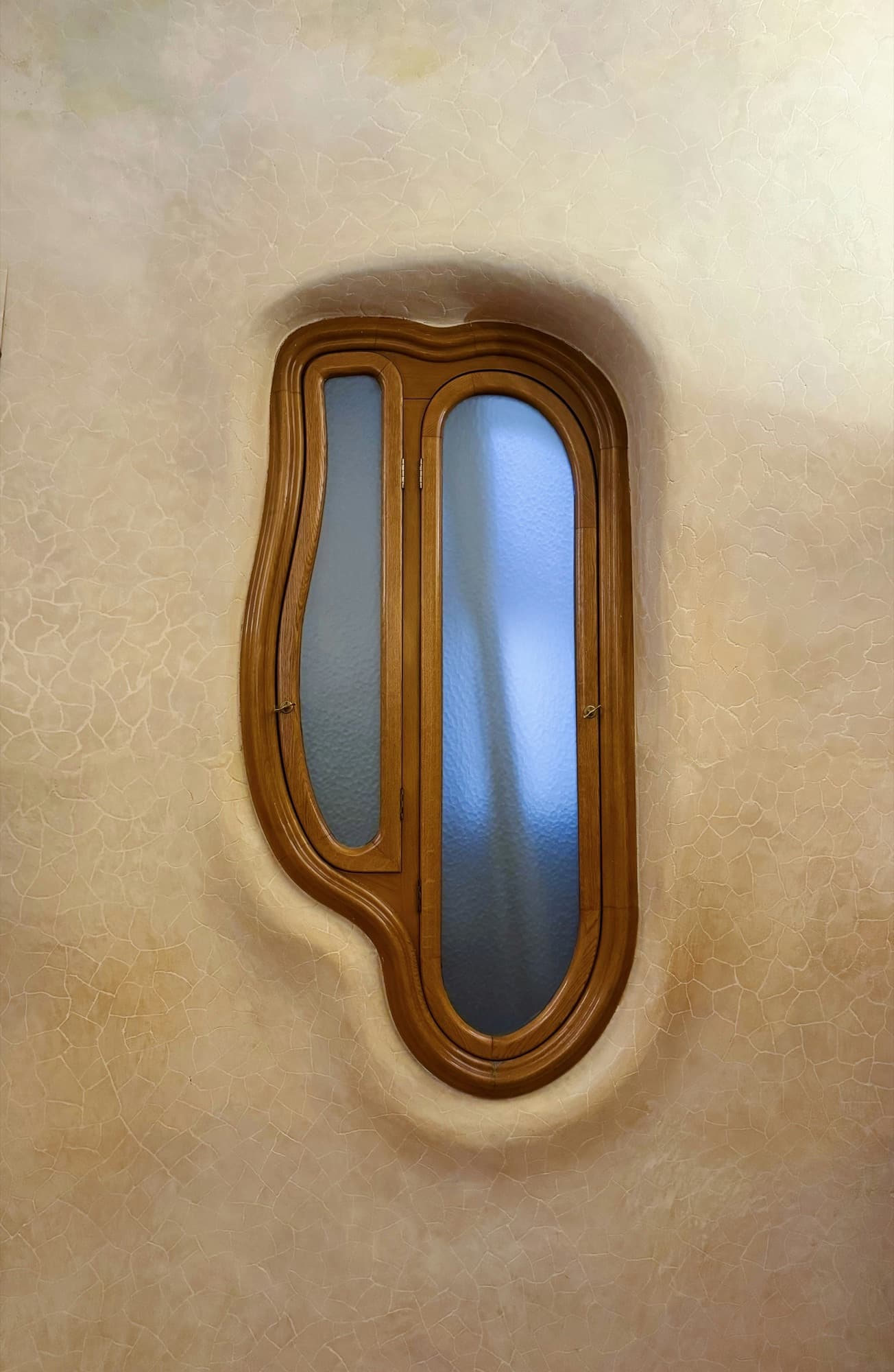 Curved wooden window with obscure textured glass set into a cream plaster wall