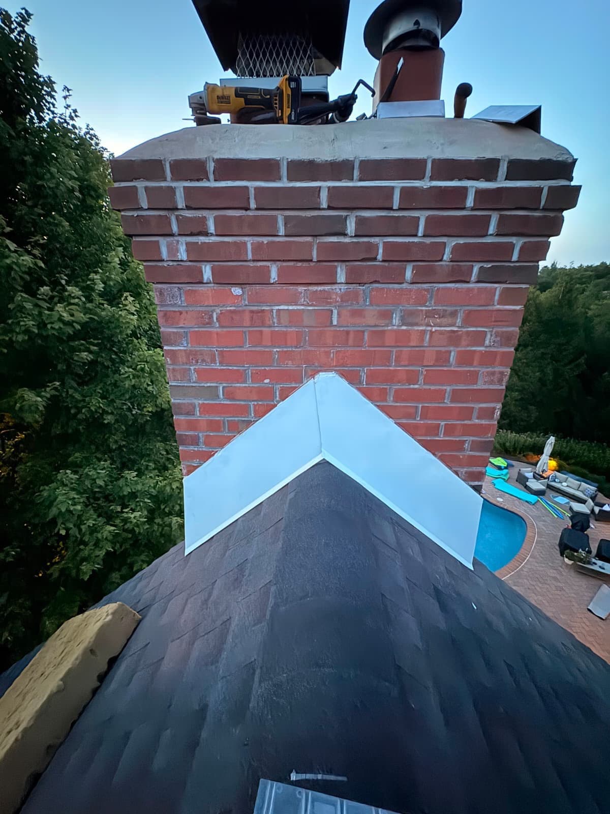 Sheet-metal cricket and step flashing built in behind a masonry chimney on a New Jersey roof — the metalwork that reaches the end of its life long before a durable roof covering does