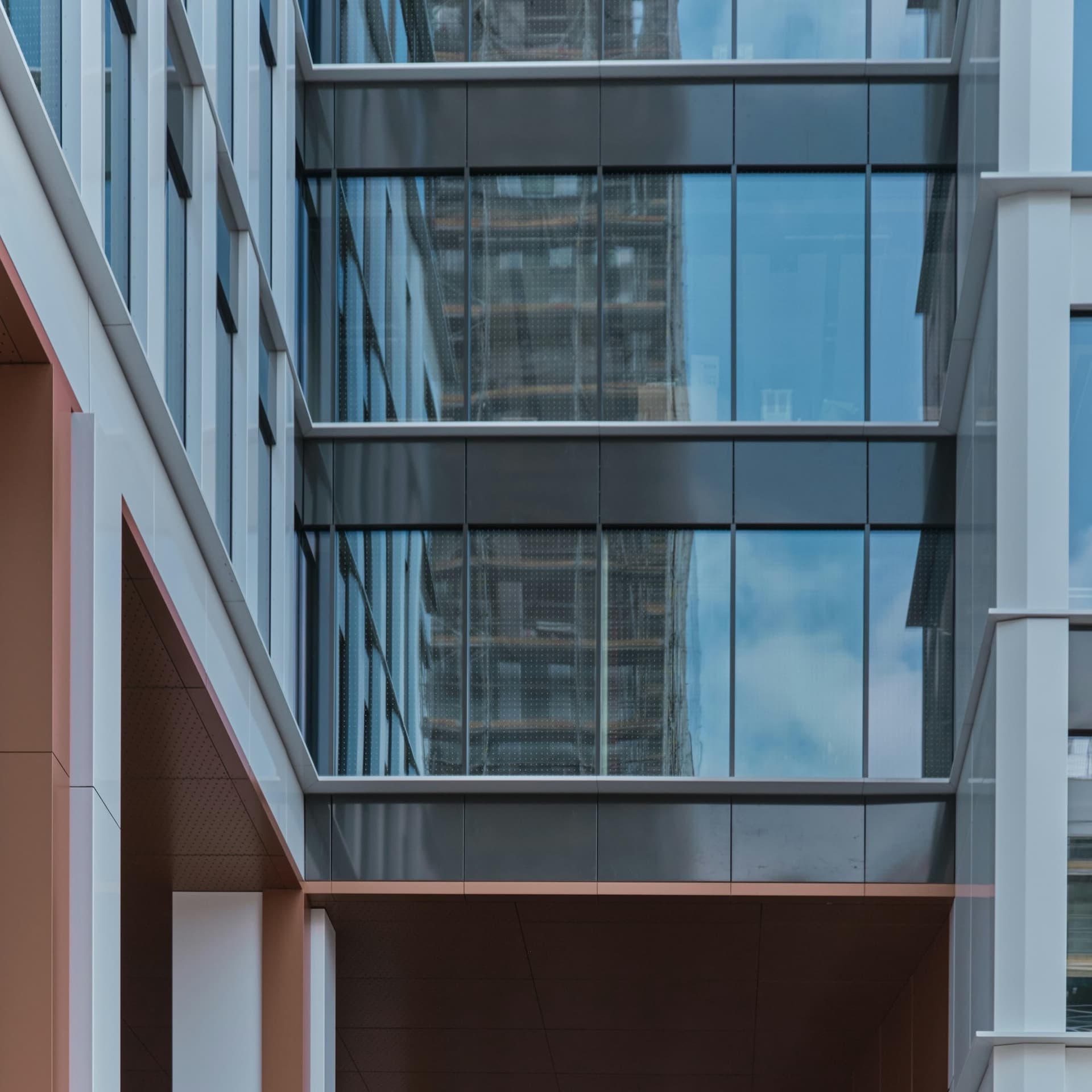 Office building glass curtain wall between dark spandrel panels, reflecting a building under construction