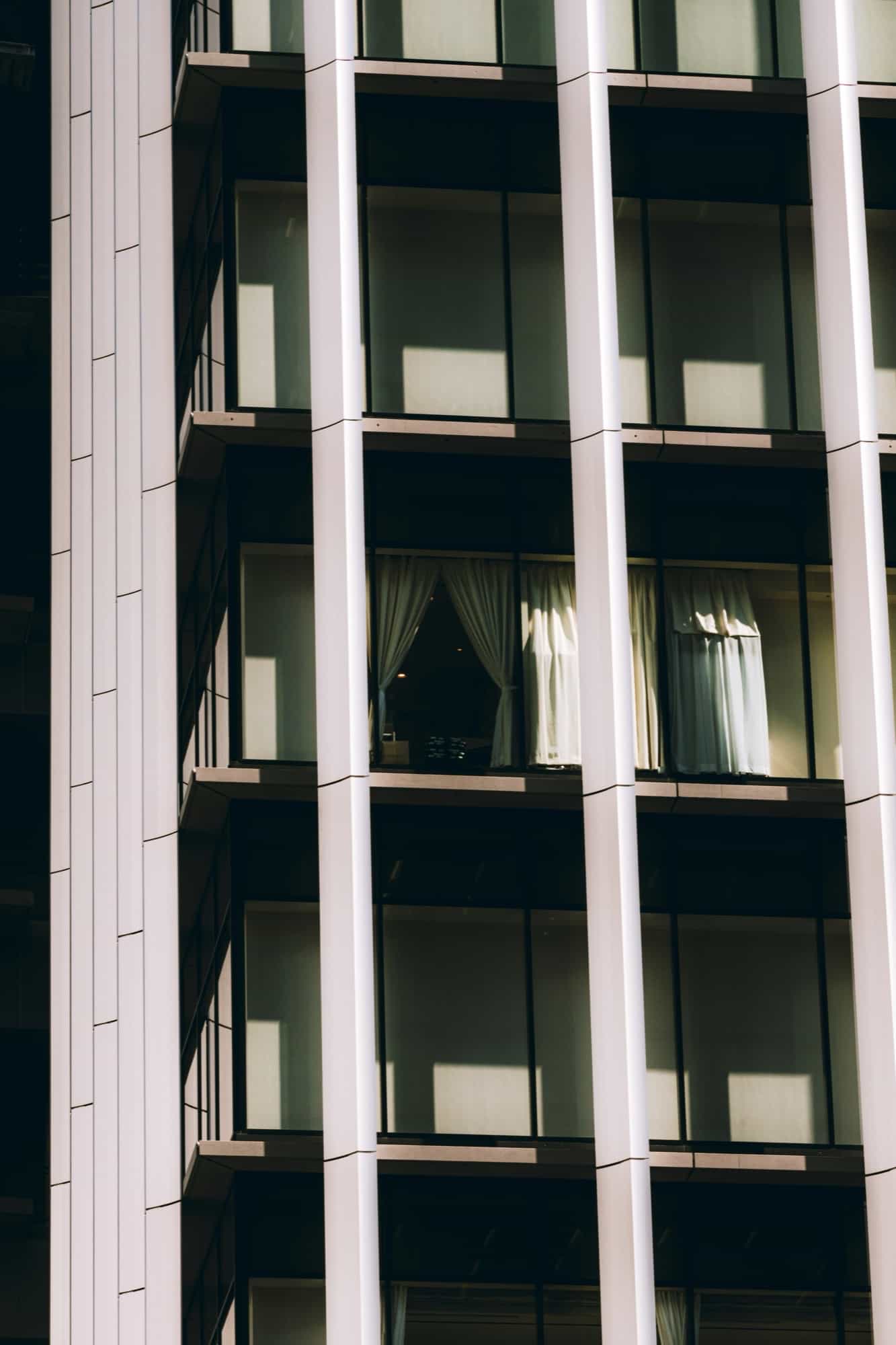 High-rise facade of floor-to-ceiling glass window bays between white vertical fins