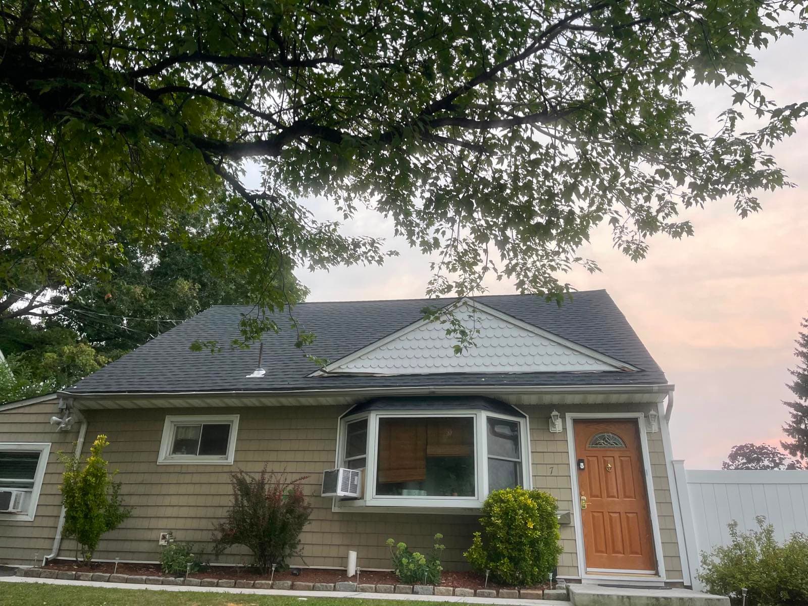 Finished charcoal architectural shingle roof on a shake-sided Cape in Parlin, NJ at dusk, with the white scalloped gable accent kept and a new white gutter run along the eave
