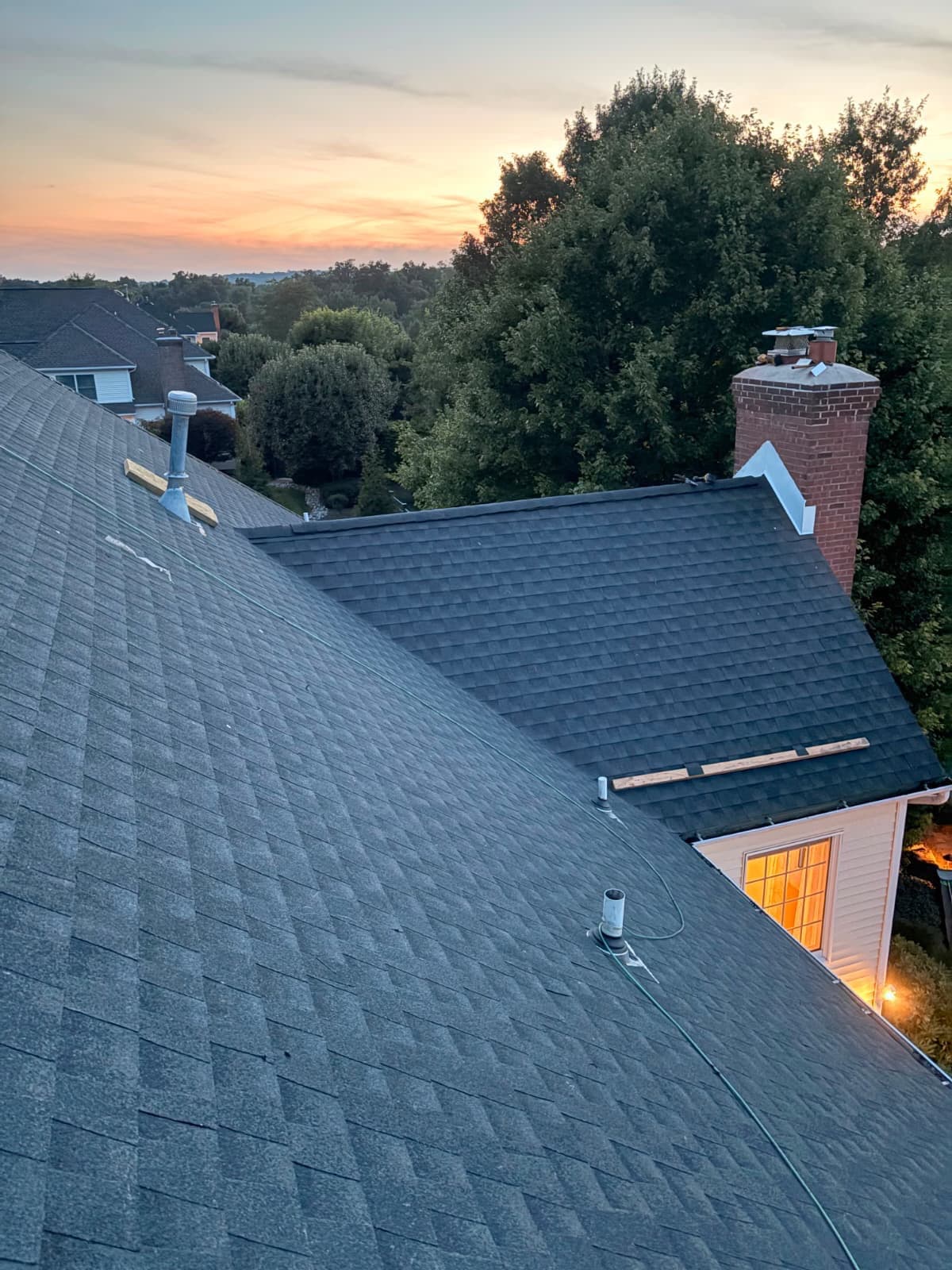 A finished asphalt shingle roof at dusk on a Saddle River, NJ home — the covering an aerial underwriting image scores, with the chimney flashing, roof vent and pipe boots that only an on-roof inspection resolves