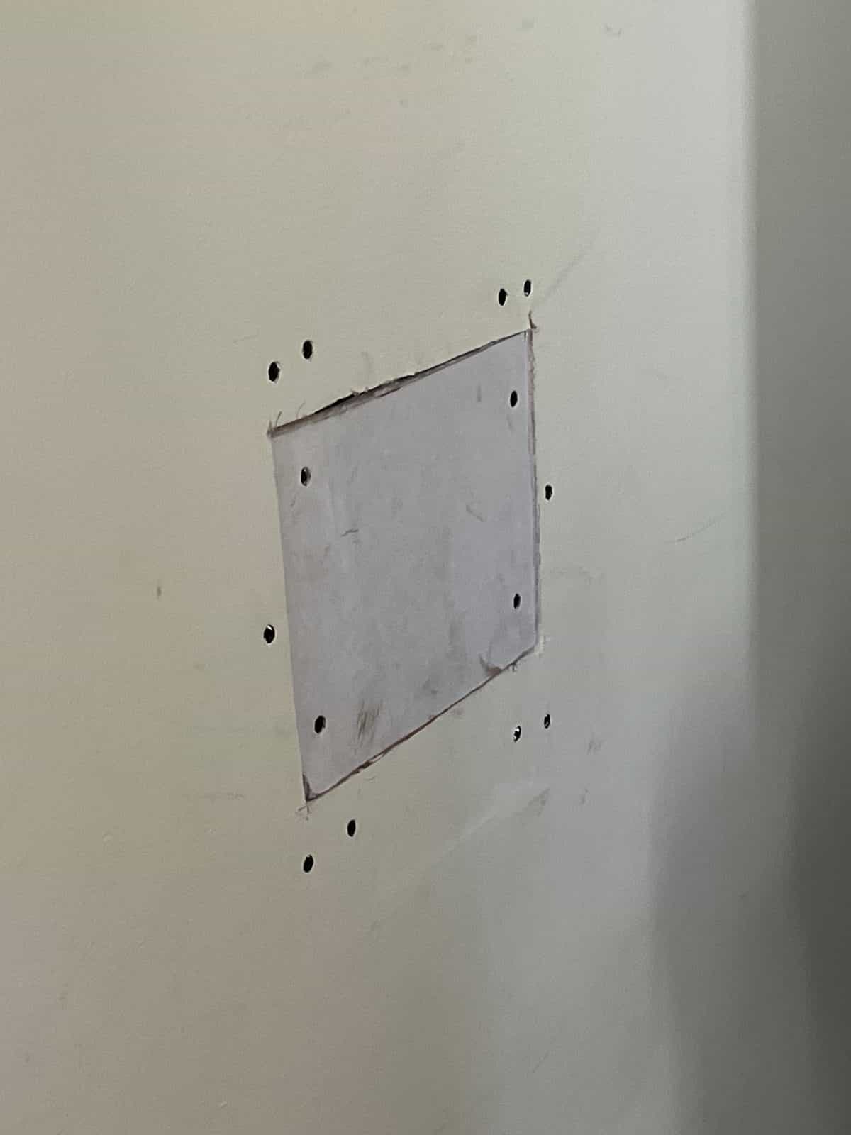 Square drywall patch screwed into a wall, ready for tape and joint compound