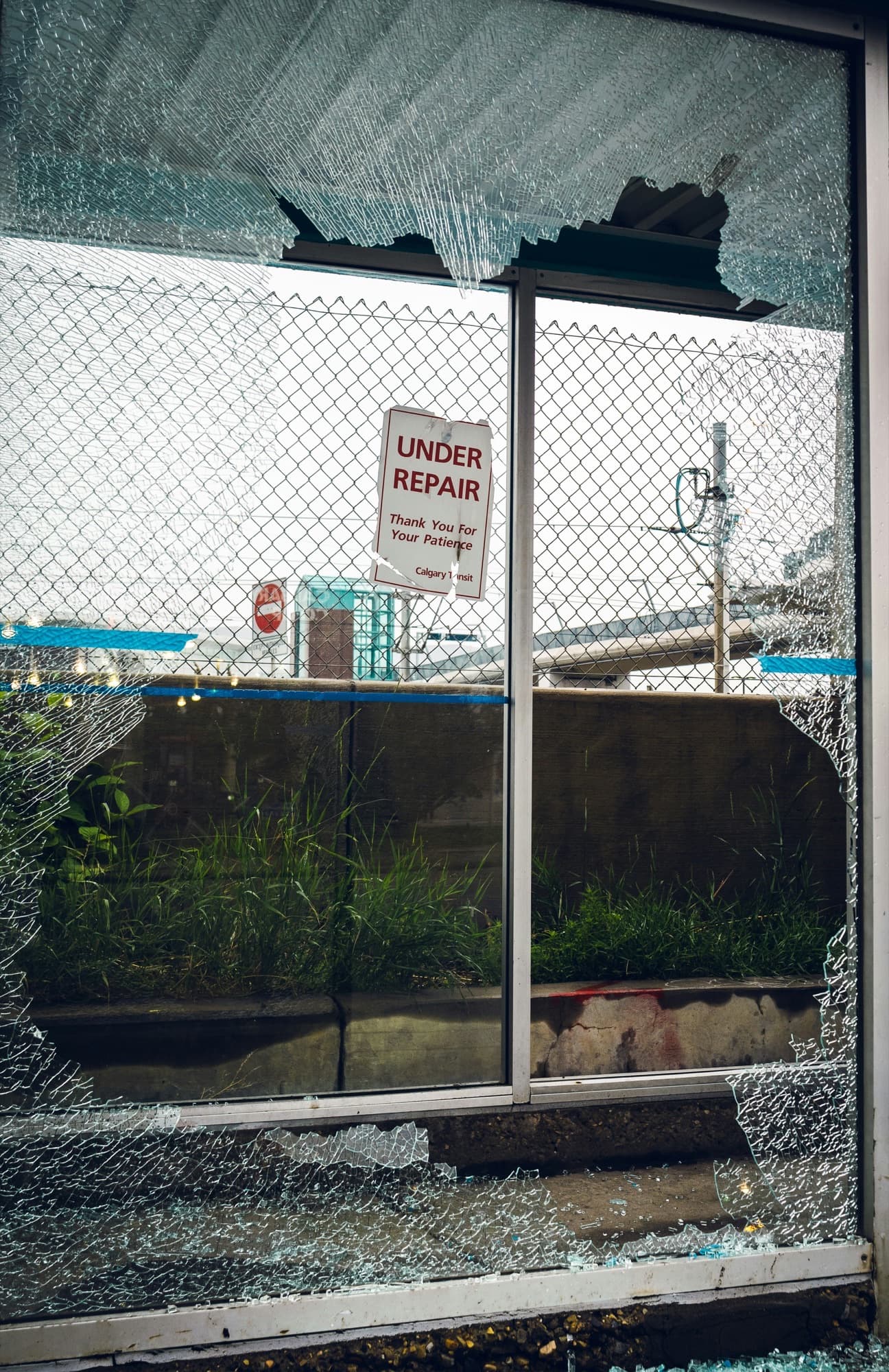 Shattered glass panel with an under-repair sign on a chain-link fence behind it