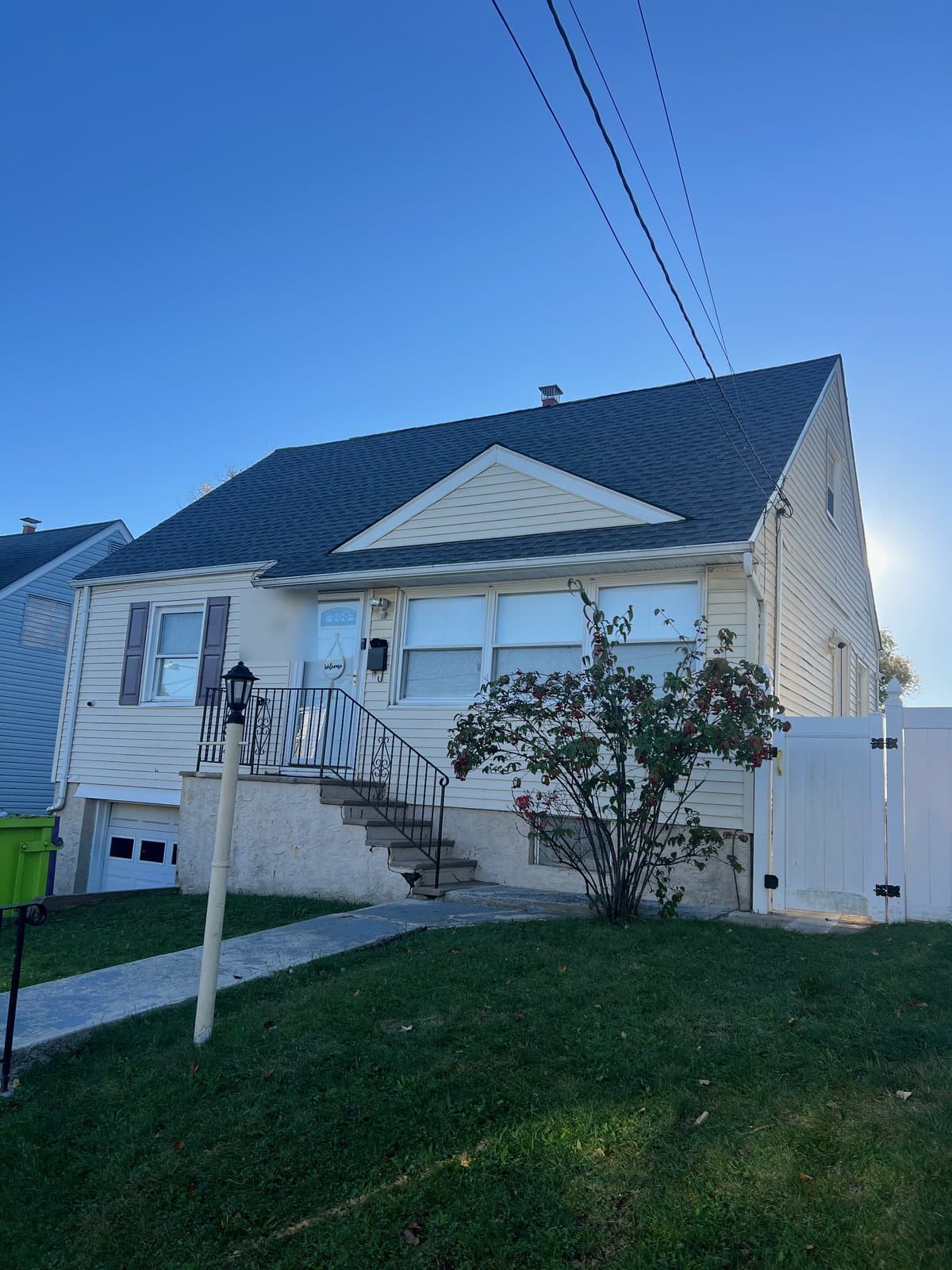 Street side of the finished Passaic, NJ Cape Cod: dark grey shingles from the eaves to the ridge, a small gable above the front steps, a capped chimney at the peak