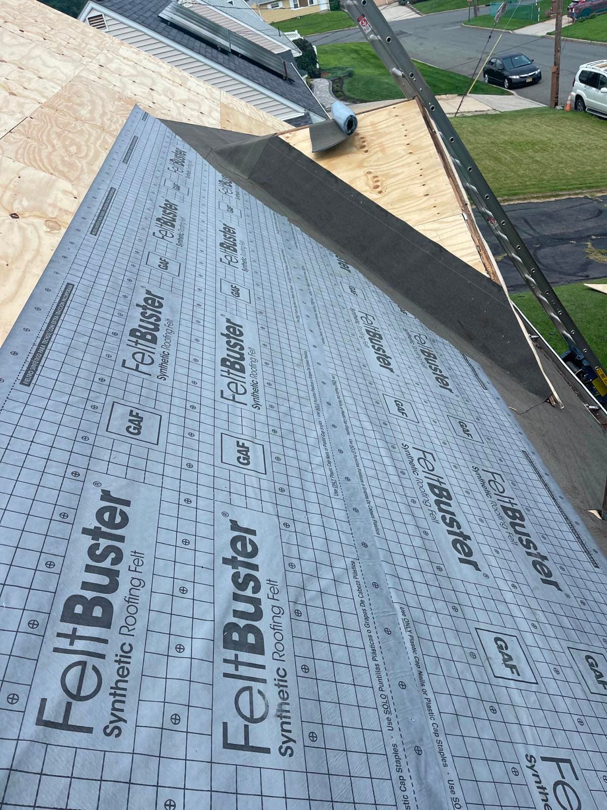 GAF FeltBuster synthetic roofing felt rolled out over new plywood decking on a Parlin, NJ hip roof, capped along the hip and fastened with plastic cap nails