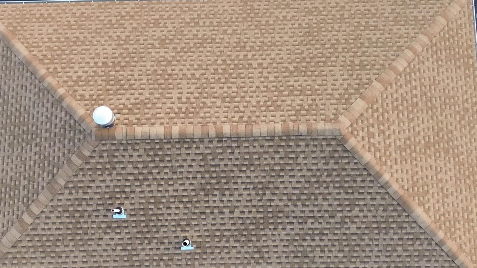 Overhead view of a finished tan architectural shingle hip roof in Lodi, NJ, ridge cap running the full length and a turbine vent set at the peak