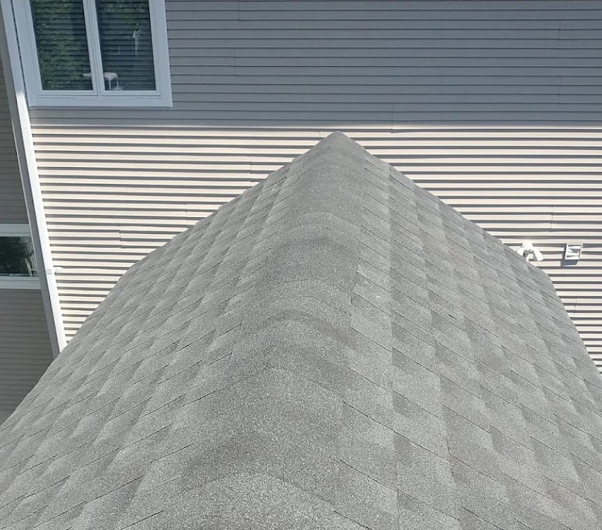 Completed light grey architectural asphalt shingle hip roof on a Rutherford, NJ home, ridge cap running to the peak where the lower roof plane meets a two-tone sided wall