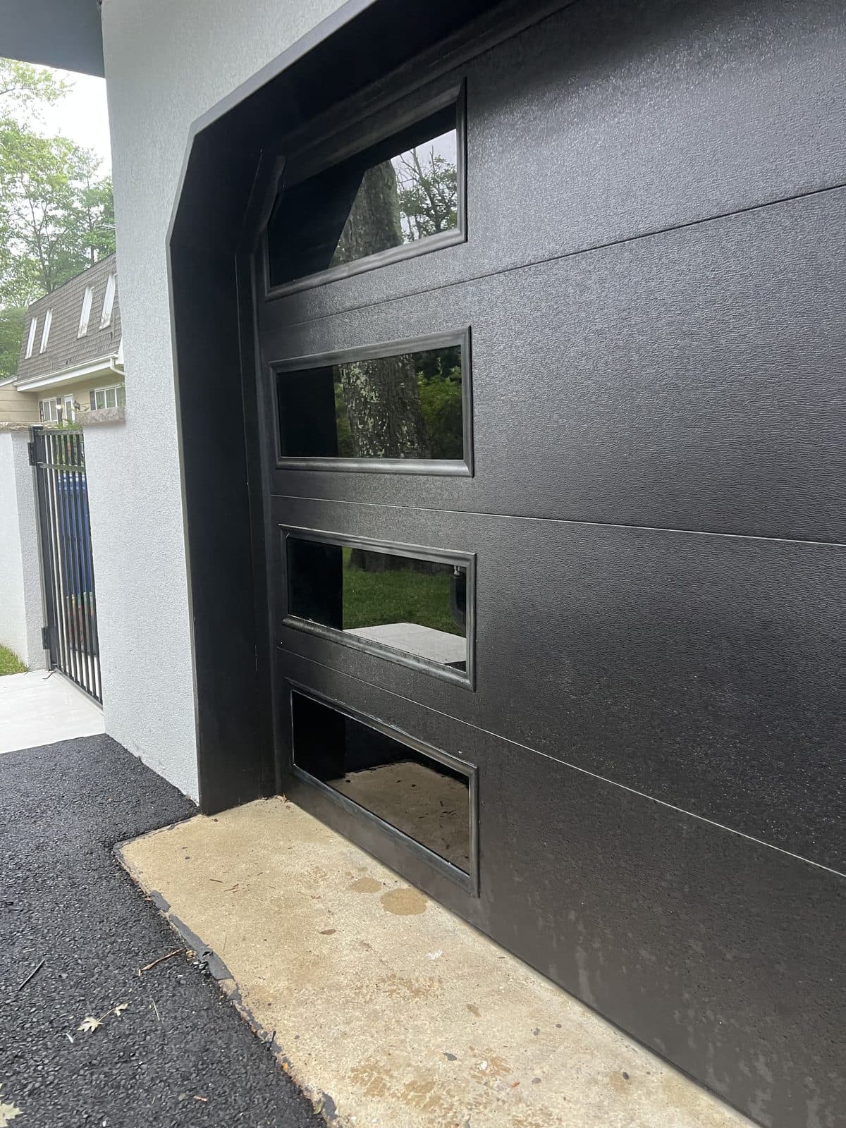 Contemporary flush black door with a stacked column of four rectangular glass vision lites on a modern stucco Garfield, NJ home, by Precision Windows & Roofing