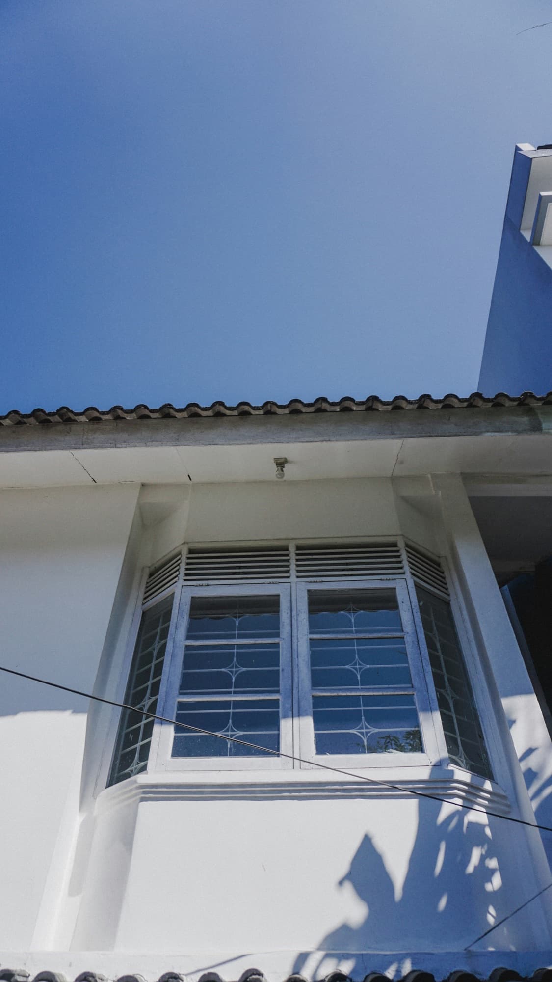 White bay window with decorative grilles under a tiled roof edge, seen from below against a blue sky