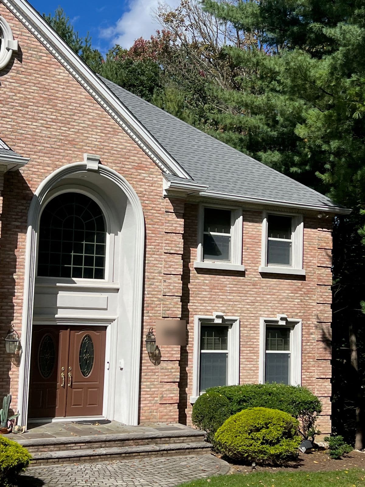 Front entry of a brick colonial in Franklin Lakes, NJ with an arched surround and double doors, under a new gray architectural shingle roof