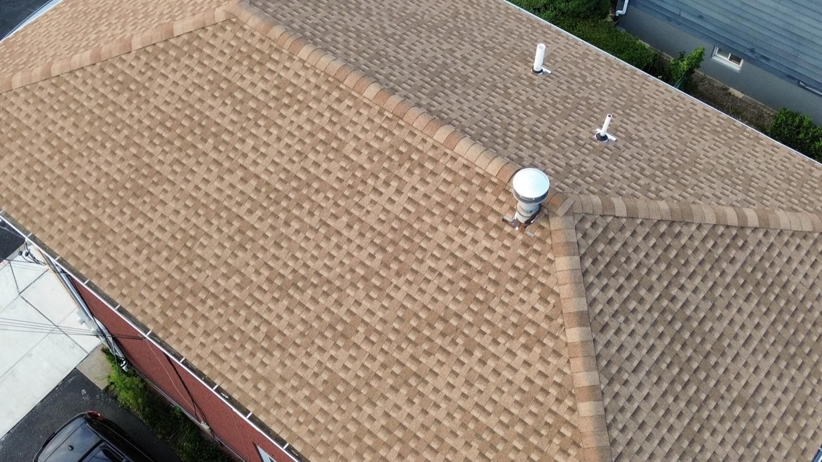 New white seamless gutters run along the eave of a completed tan shingle hip roof on a brick building in Lodi, NJ