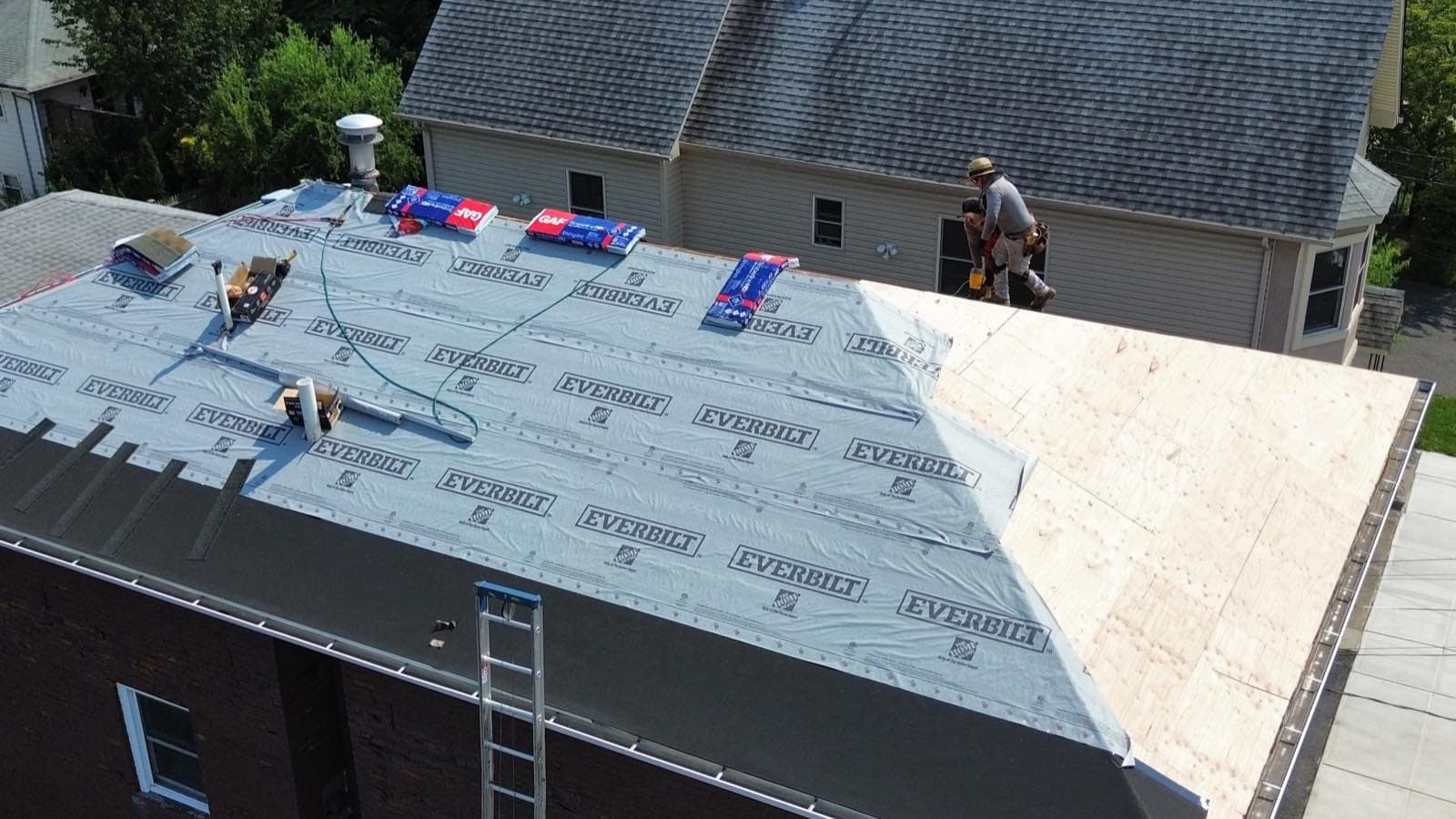 Precision crew on a Lodi, NJ roof laying synthetic underlayment over fresh plywood decking, with GAF shingle bundles staged along the ridge