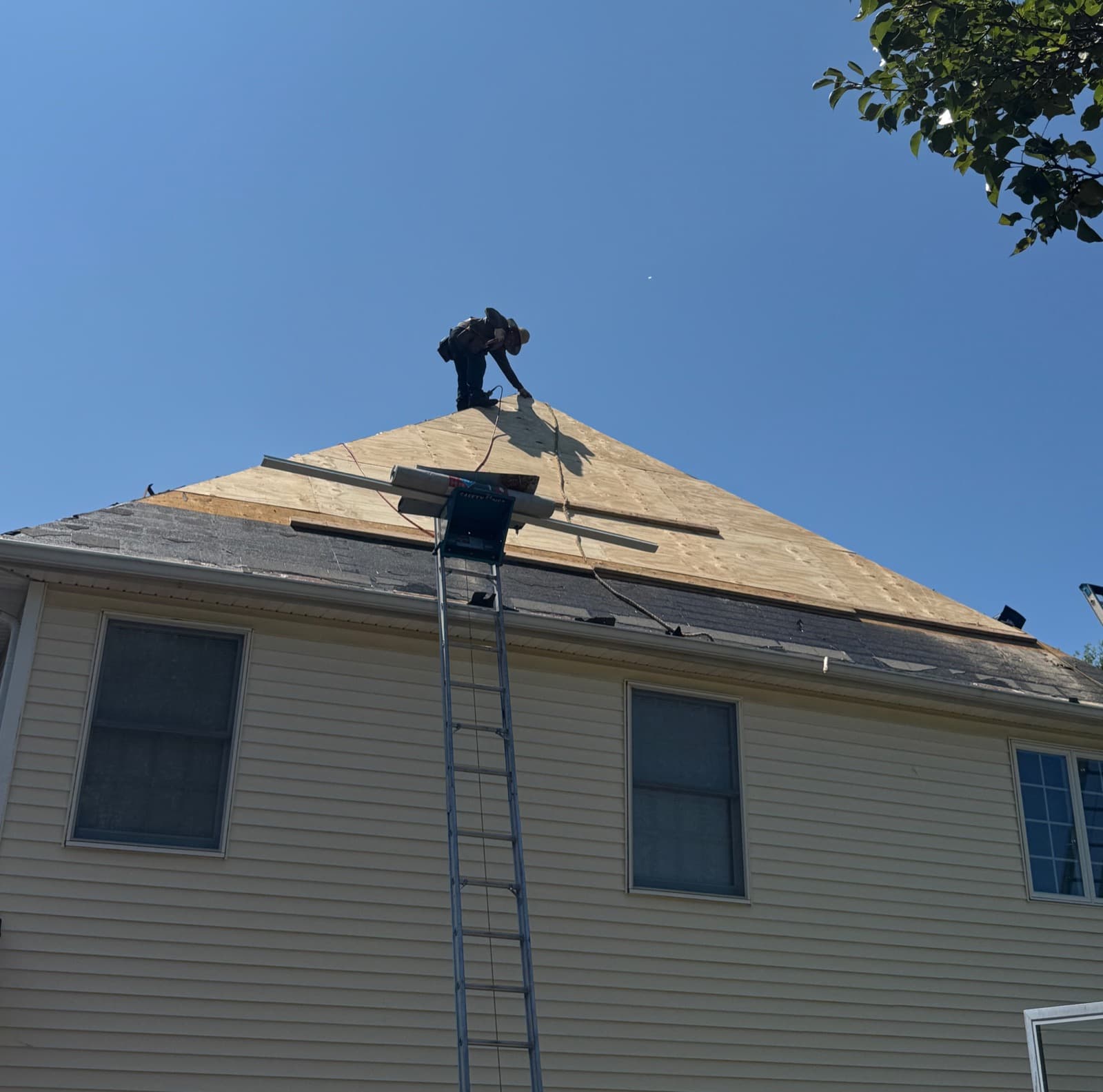 Hip roof mid tear-off on a New Jersey home, new plywood decking down across the upper slope and a ladder hoist set at the eave