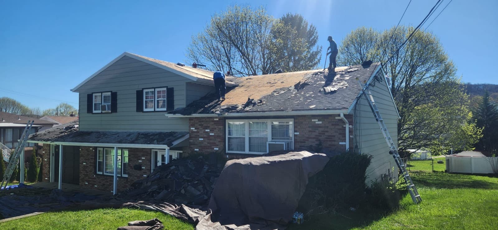 Old asphalt shingles coming off a New Jersey roof in one working day, a single slope stripped to the deck while the next stays covered