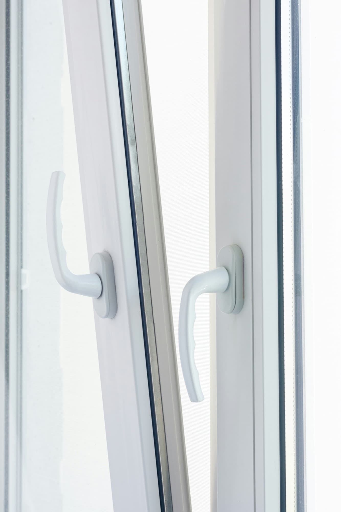 Close-up of two white vinyl window sashes with lever handles, one tilted open