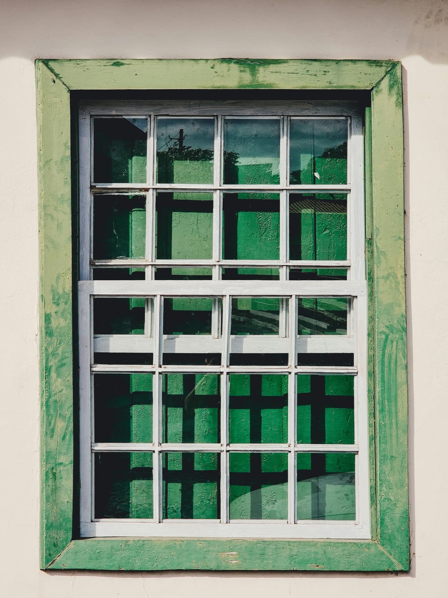 Divided-lite double-hung wood window in a weathered green-painted frame on a cream wall