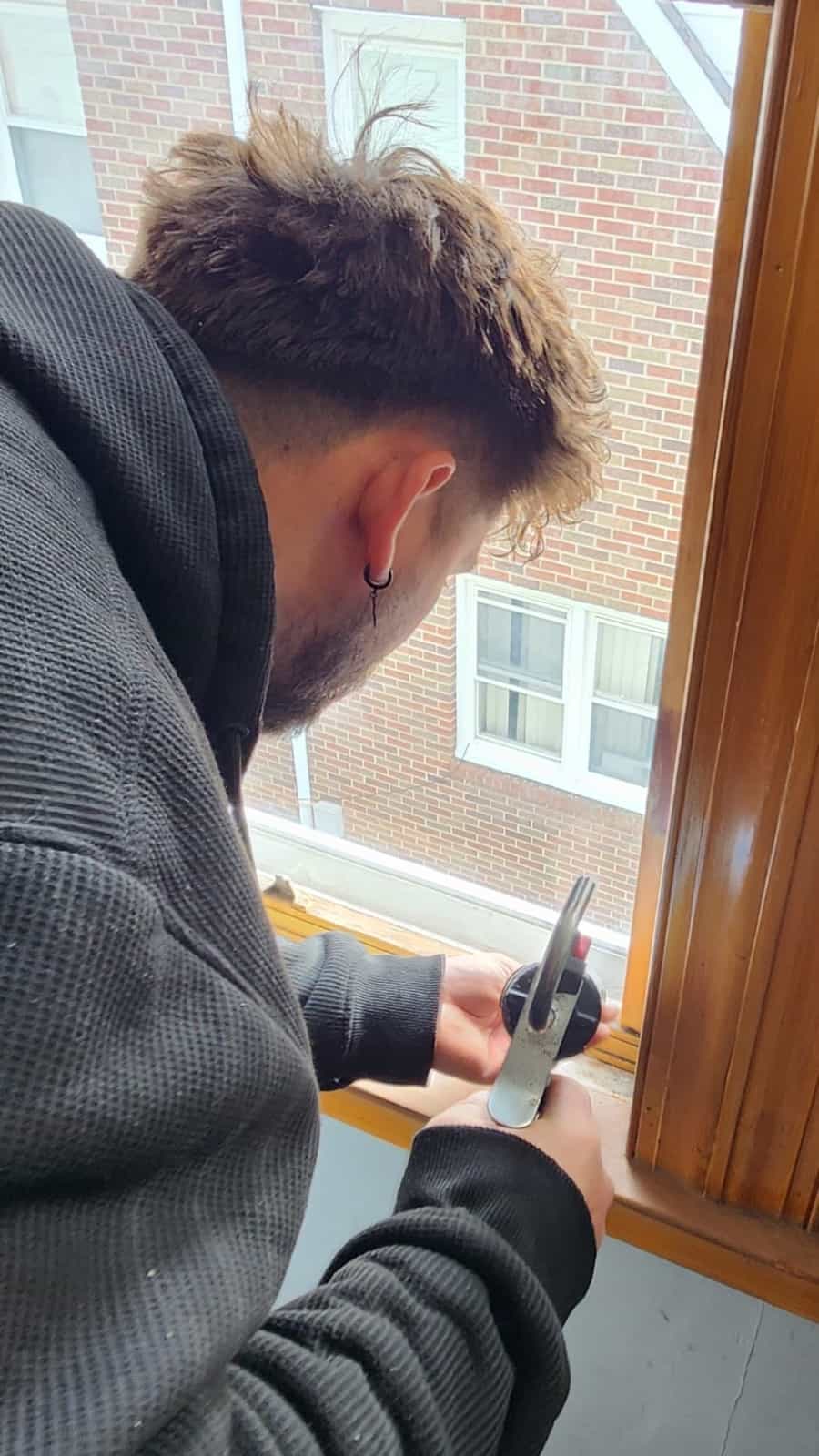 Technician holding a suction-cup glass lifter at a stained-wood window opening