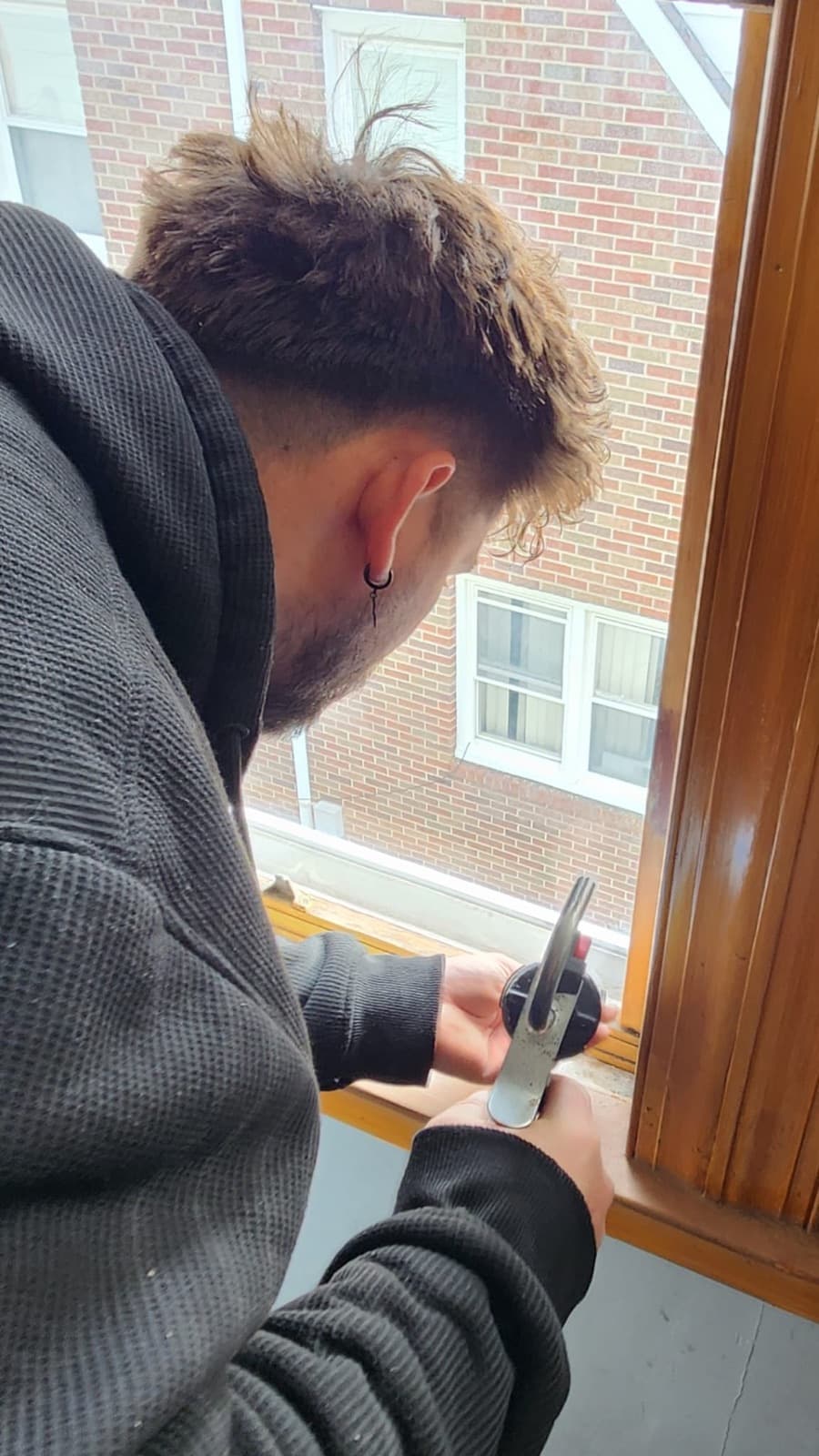 Precision Windows & Roofing technician re-glazing a wood window sash on site in New Jersey, working glazing compound into the rabbet with a putty knife